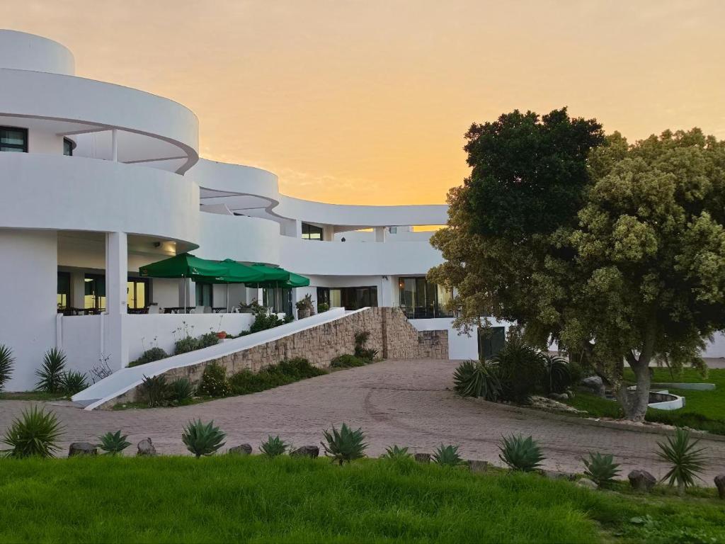 a large white building with a tree in front of it at St Helena Bay Hotel in St. Helena Bay