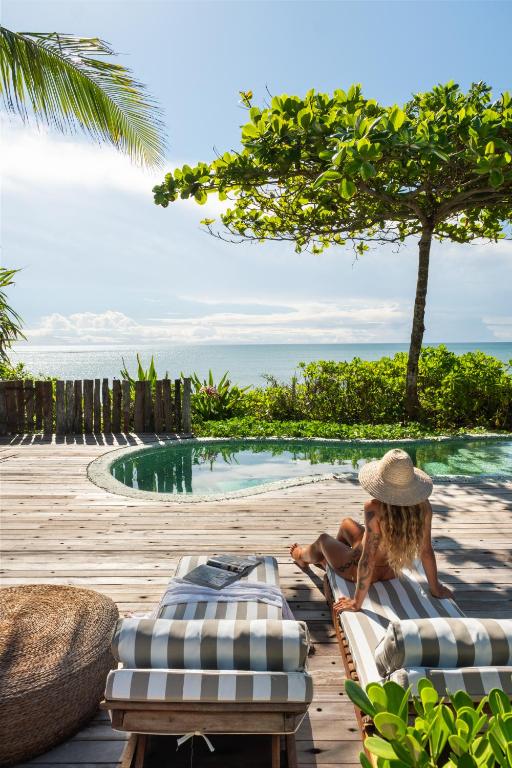 a woman sitting on a chair next to a swimming pool at Casa do Amor Caraíva in Caraíva