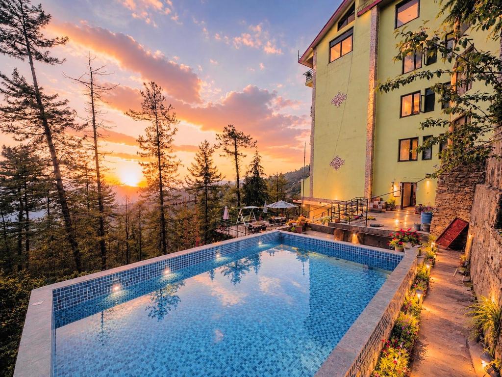 a swimming pool in front of a building with a sunset at Aachman Nature Valley Resort MASHOBRA in Shimla
