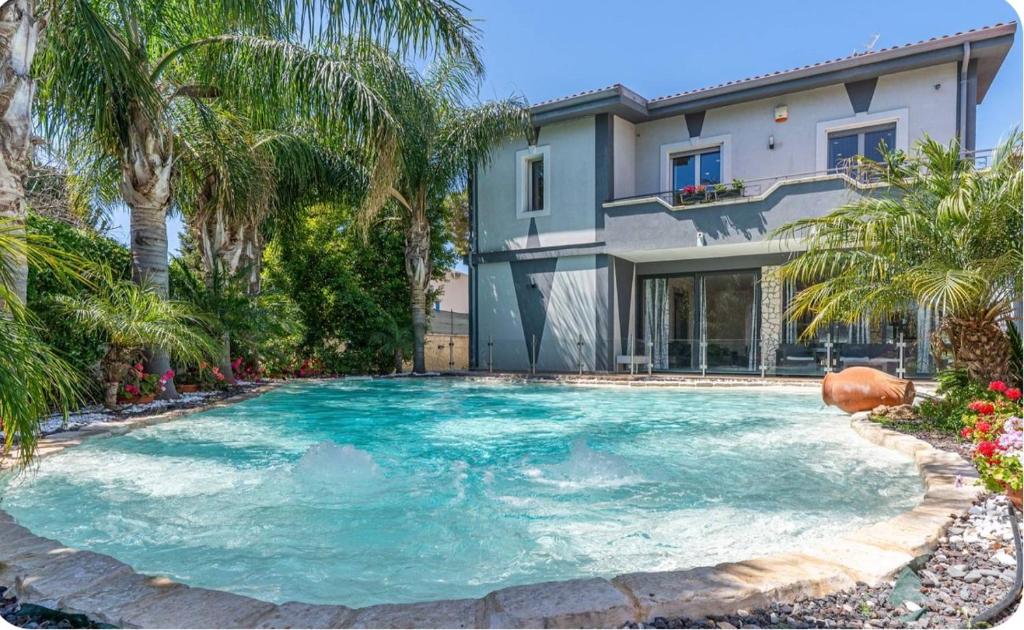 a swimming pool in front of a house with palm trees at Villa Joel in Fontane Bianche