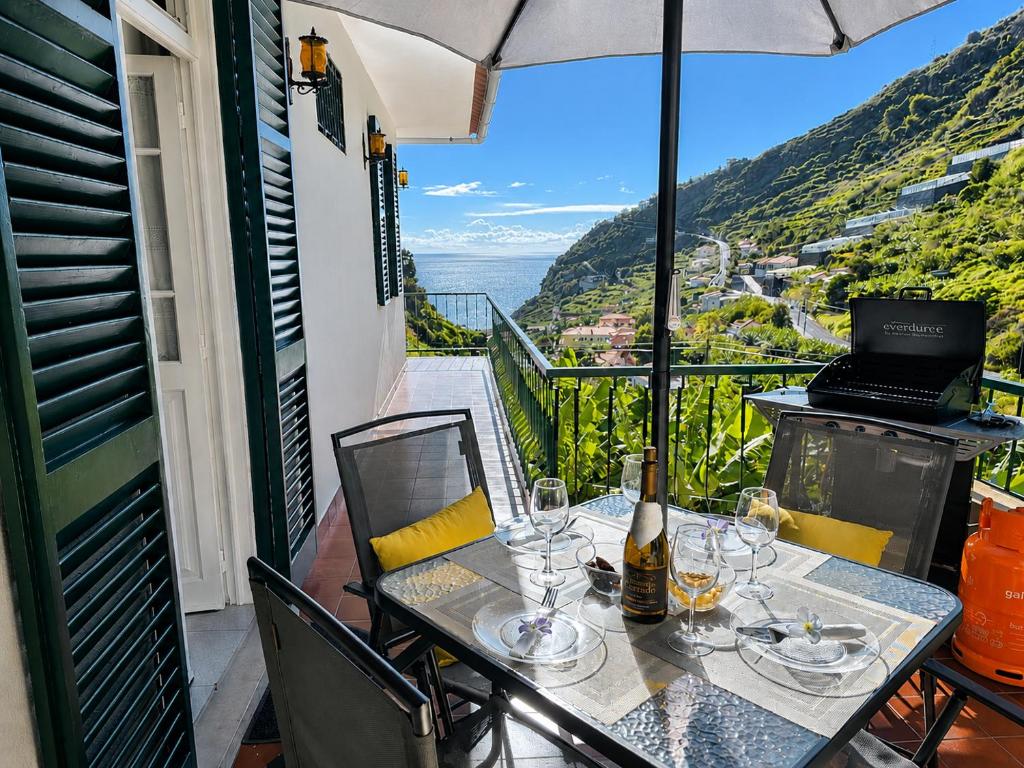 a table with wine glasses and an umbrella on a balcony at Banana Lovers - Farm View in Ribeira Brava