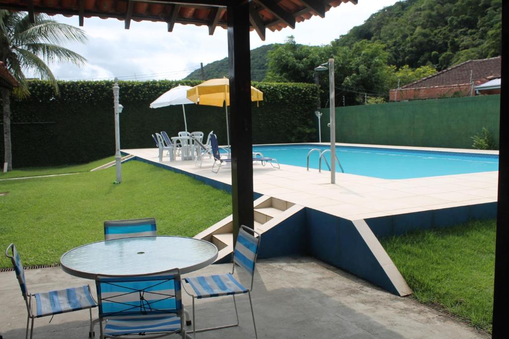 a table with chairs and an umbrella next to a pool at O Melhor Chalé da Praia do Guaiúba, com Churrasqueira e Piscina Gigante in Guarujá