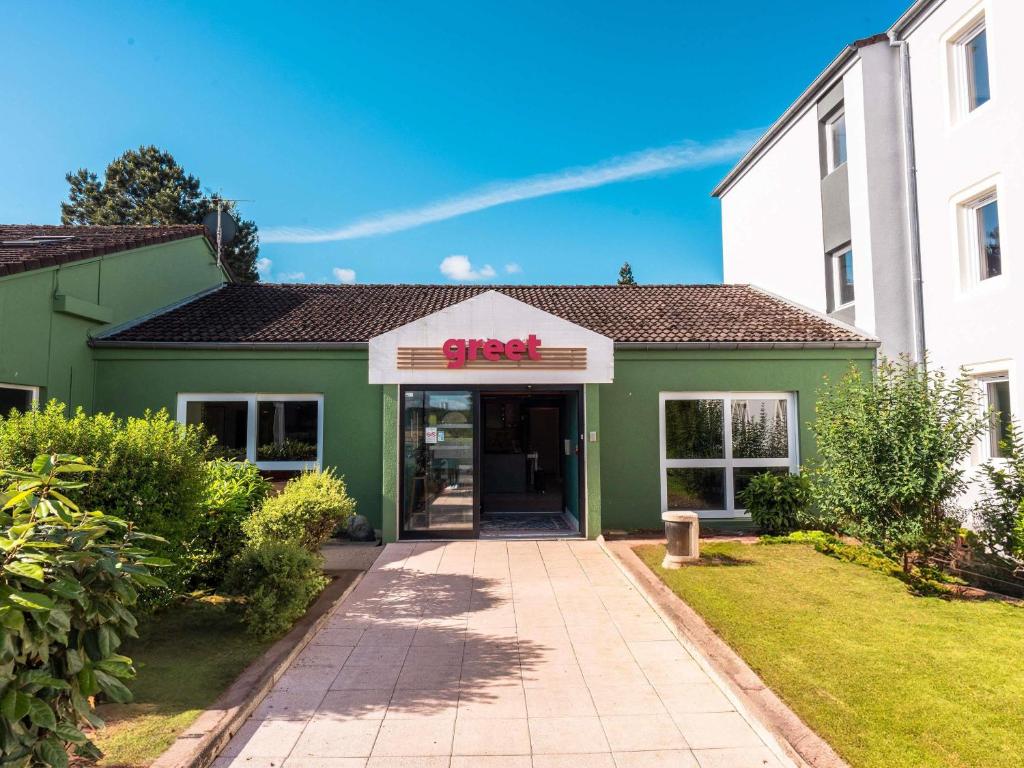 a green building with a sign that reads stop at greet Hôtel Montbéliard in Montbéliard