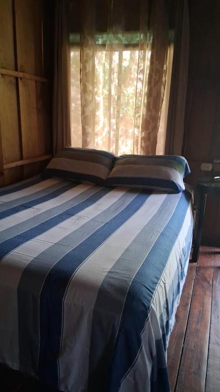 a bed with a blue and white striped blanket and a window at La cabaña de Eugenio in Convento