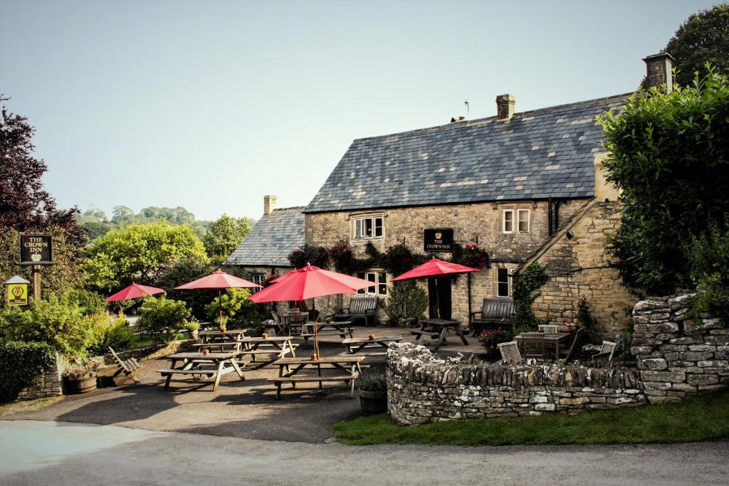 un restaurante con mesas y sombrillas frente a un edificio en The Crown Inn en Rodmarton