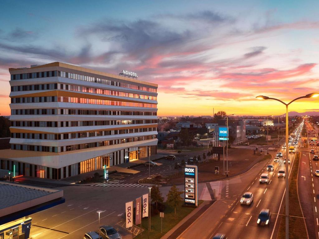 Novotel hotel with orange-and-white facade and adjacent RIX signage on a busy multi-lane road at sunset at Novotel Zagreb in Zagreb
