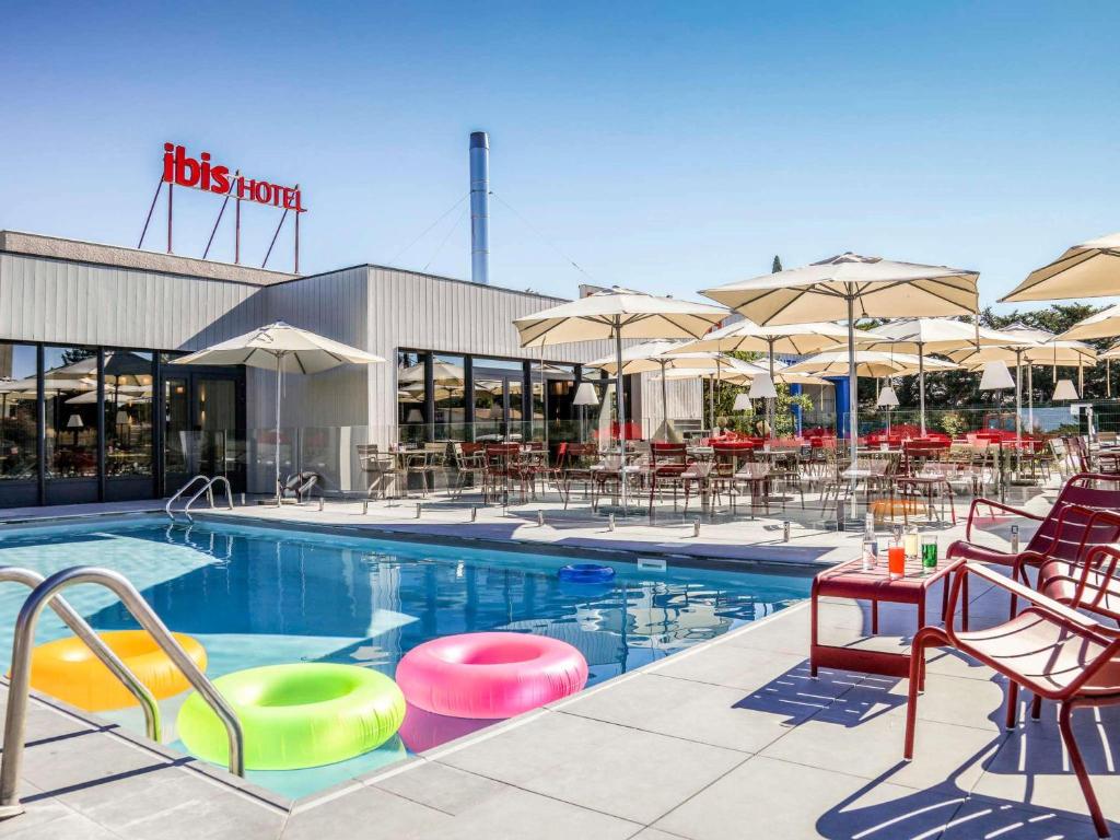 a swimming pool with chairs and tables and umbrellas at ibis Orange Centre Echangeur A7 A9 in Orange