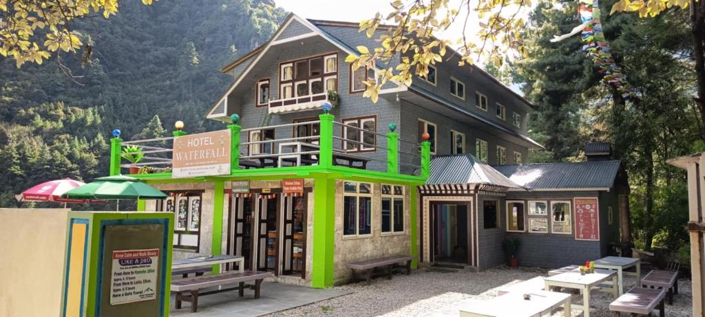 a building with green trim with picnic tables in front of it at Hotel Waterfall Benkar in Phakding