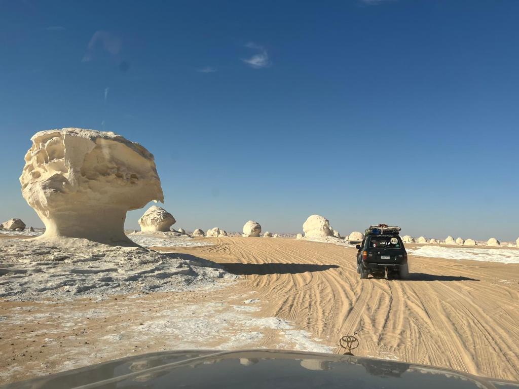 a car driving through the desert with a large rock at White Desert Experience in Bawati