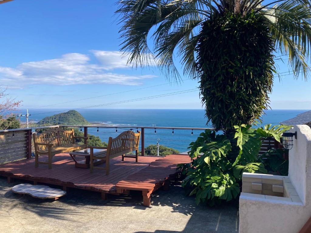 a wooden deck with two benches and the ocean at 丘の上の小さなスローリゾート フェニックスの宿 in Miyazaki