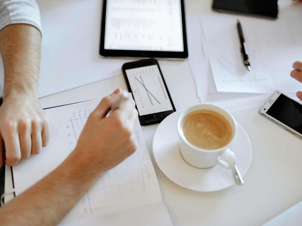A shared worktable holds coffee, stationery and several mobile devices.