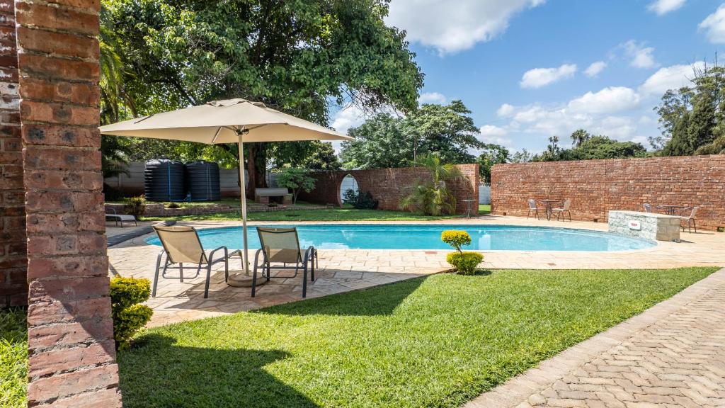 an umbrella and chairs next to a swimming pool at 36 Alexander Guesthouse,Highlands,Harare in Highlands