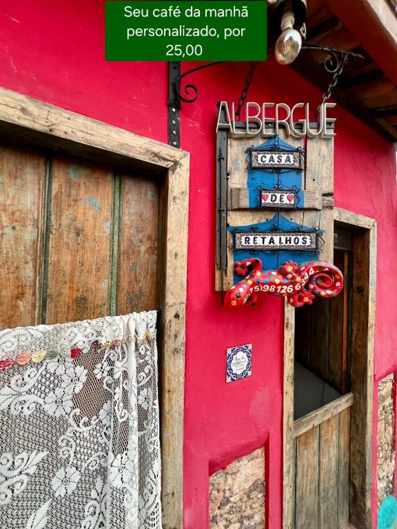 a red door of a red building with a sign on it at CASA DE RETALHOS Boutique Albergue, casaril histórico, com 5 suítes individuais e cozinha coletiva, no coração da vila de Igatu-Ba, que preserva fortes traços culturais da época do garimpo, venha viver uma experiência única! in Igatu