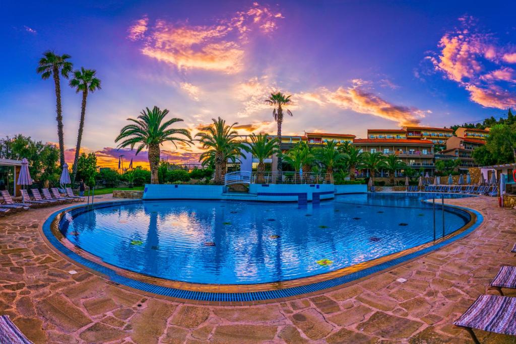 une piscine dans un complexe avec des palmiers et un coucher de soleil dans l'établissement Lagomandra Hotel and Spa, à Lagomandra