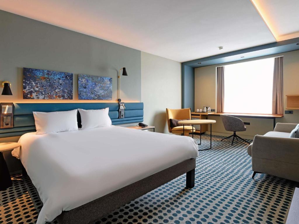 ein Hotelzimmer mit einem großen Bett und einem Stuhl in der Unterkunft Novotel Luxembourg Kirchberg in Luxemburg (Stadt)