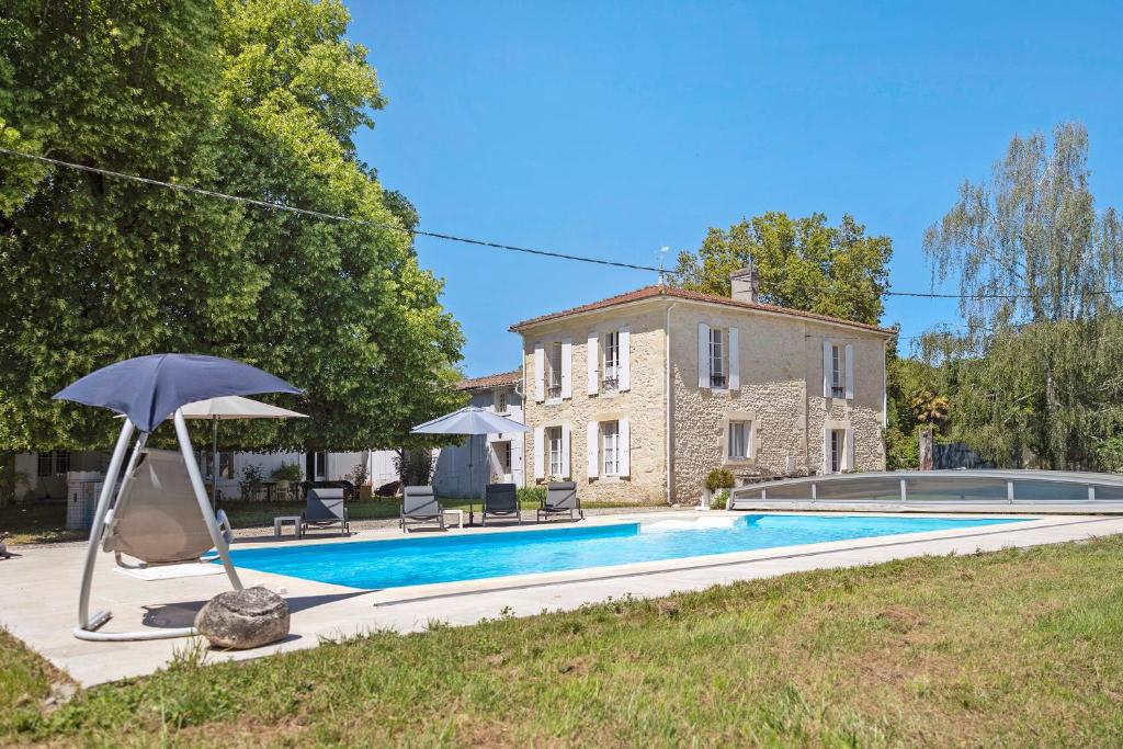 a pool with an umbrella and chairs and a house at La maison de Léandre - Medoc in Saint-Seurin-de-Cadourne