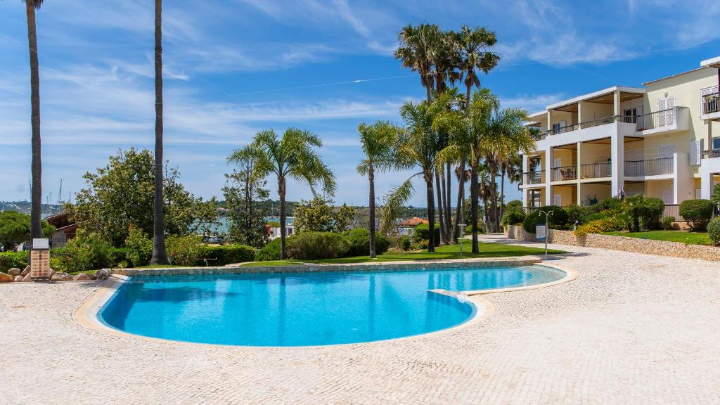 a swimming pool with palm trees in front of a building at Clube Alvor Ria - Prime Residence in Alvor