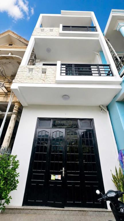 a white building with a black door and a balcony at Mubee Homestay in Hue