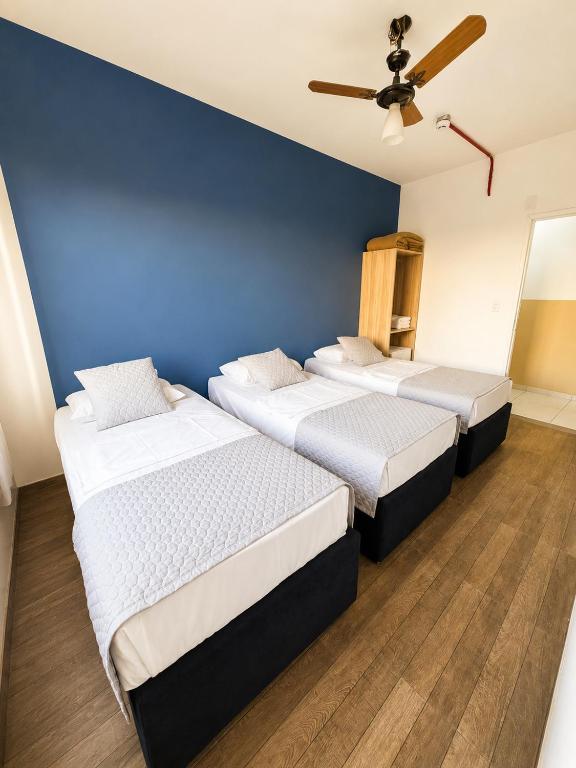 two beds in a room with a blue wall at Hotel Mão de Fatima in Aparecida