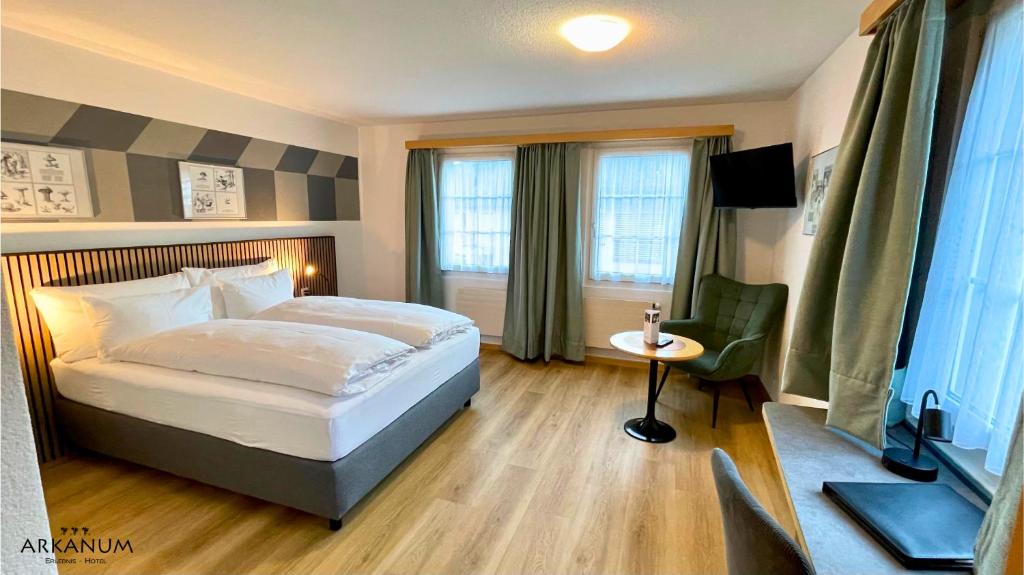a bedroom with a bed and a table and windows at Hotel Arkanum in Salgesch