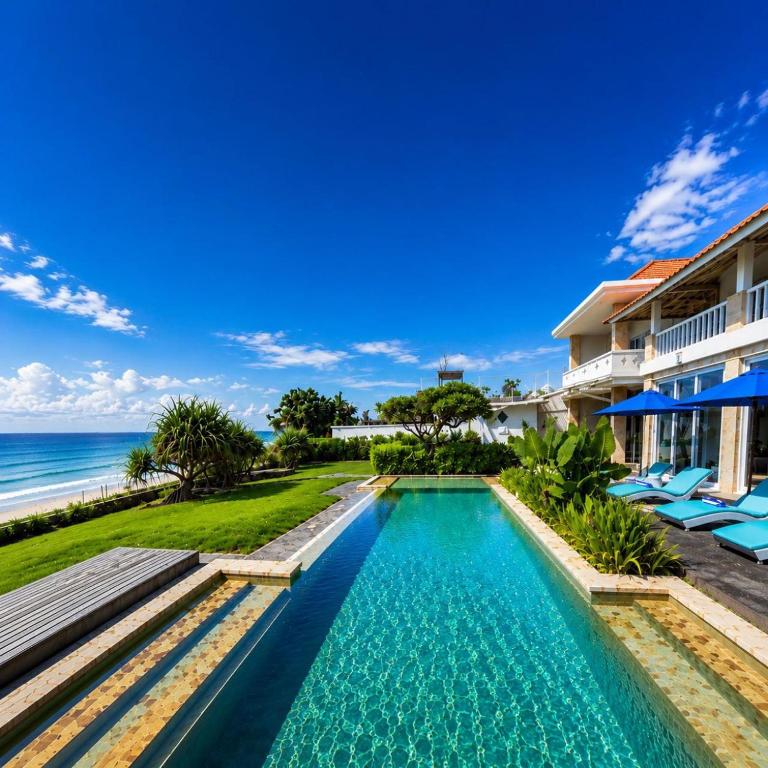a swimming pool in front of a resort with the ocean at Suzuki Villa Ketewel Beachfront in Ketewel