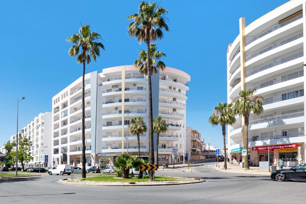 a large white building with palm trees in front of it at Rei Apartment in Quarteira