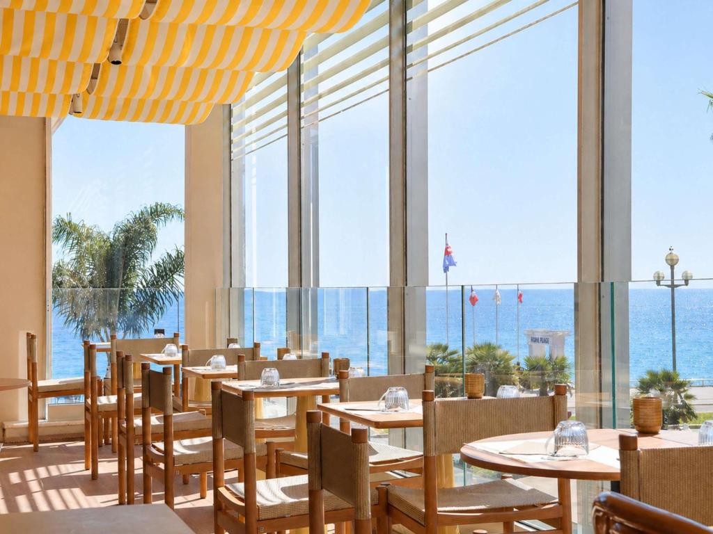 a restaurant with tables and chairs with a view of the ocean at Mercure Nice Promenade Des Anglais in Nice
