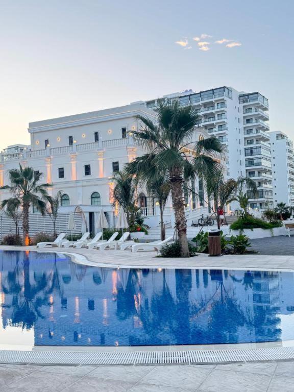 a swimming pool in front of a building with palm trees at Marcellus Iskele Resort Ceasar in Larnaca