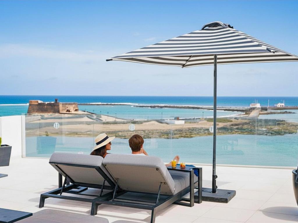 two people sitting in chairs under an umbrella at Blue Marina Suites - Boutique Apartments in Arrecife
