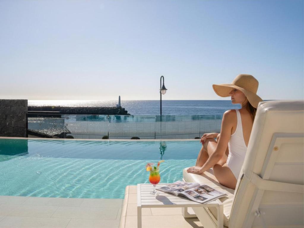 a woman sitting on a chair next to a swimming pool at Royal Marina Suites Boutique Hotel - Adults Only in Puerto Calero
