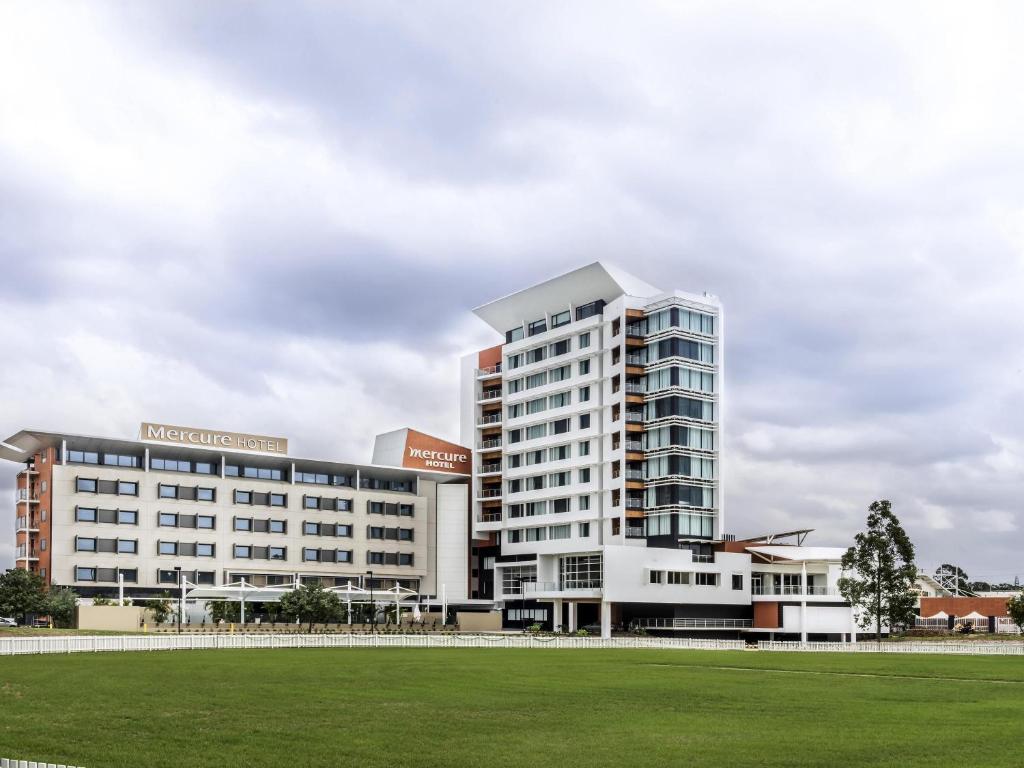 a large white building with a green field in front at Mercure Sydney Liverpool in Liverpool