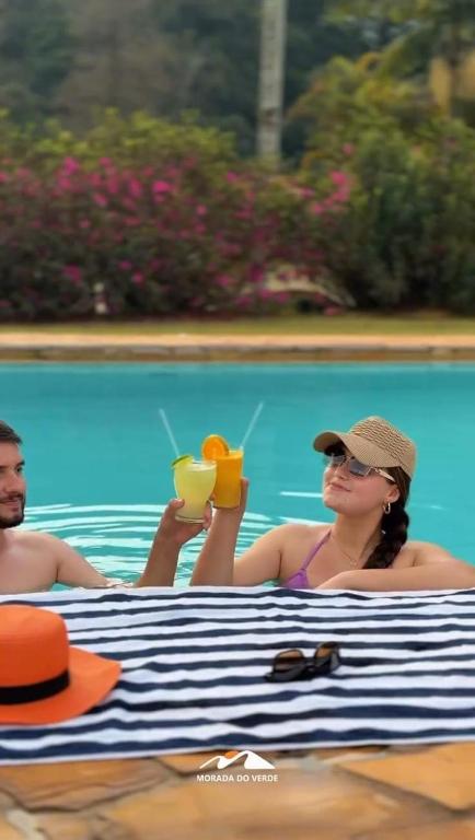 a man and a woman sitting in a pool with drinks at Hotel Fazenda Morada Do Verde in Campo Limpo