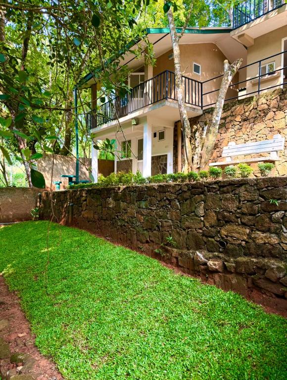 a house with a stone retaining wall and a yard at Villa Whispering Leaves Kandy in Galaha Town