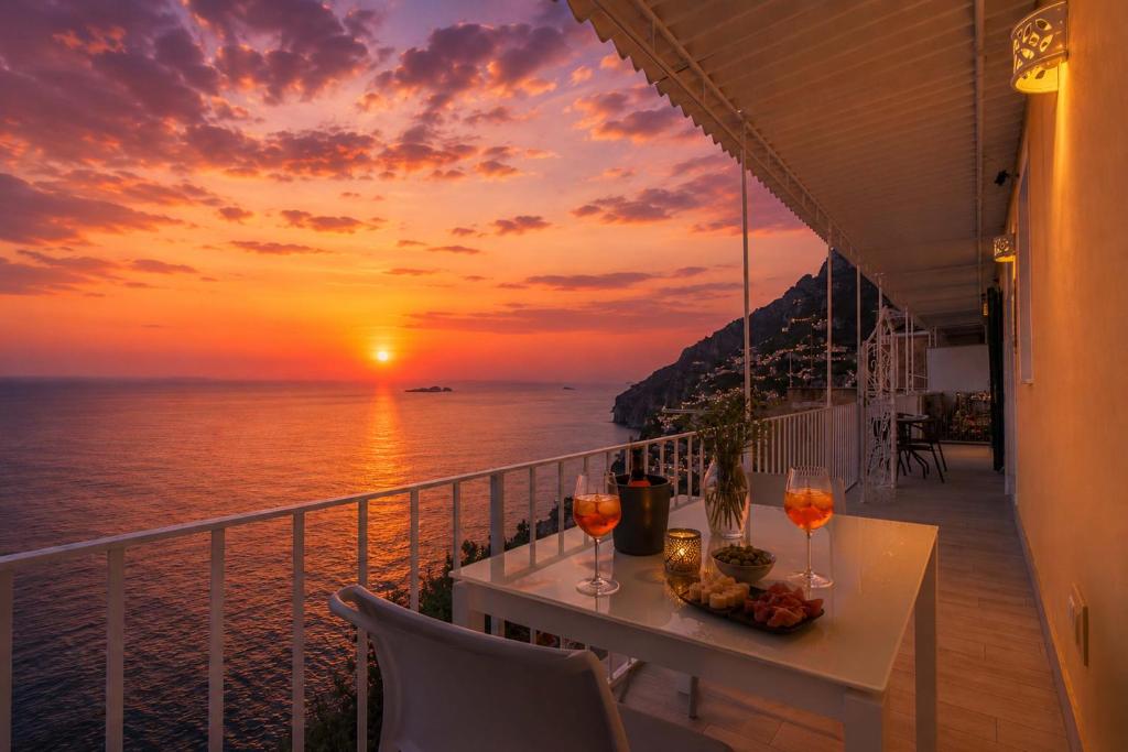 a balcony with a table with wine glasses and a sunset at Amore Rentals - Villa Anna in Positano