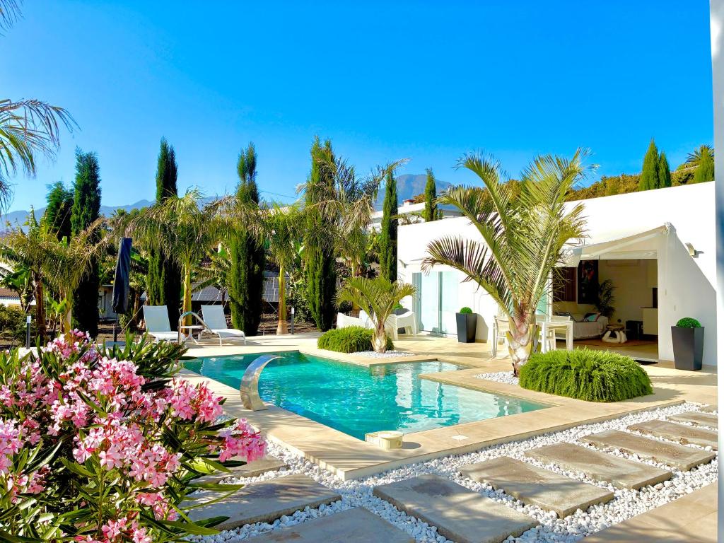 a swimming pool with palm trees and pink flowers at Casa Tajuya in Los Llanos de Aridane