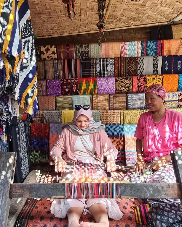 a woman sitting on a bench in a market at Greentea Hostel in Labuhanhaji