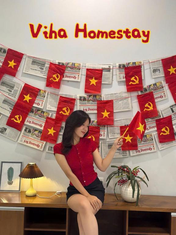a woman sitting on a desk in front of a wall with flags at Viha Homestay in Thôn Trường Giang
