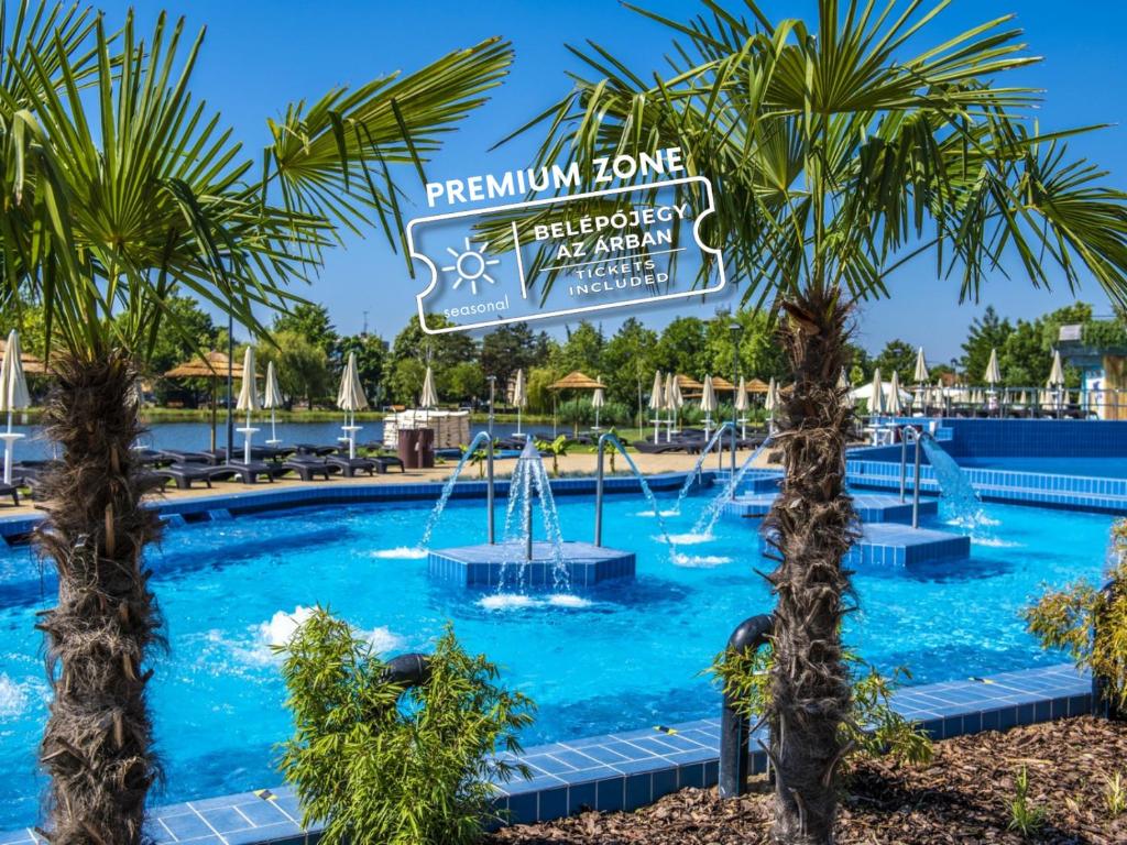 a swimming pool with palm trees in the foreground at Hungarospa Thermal Hotel in Hajdúszoboszló