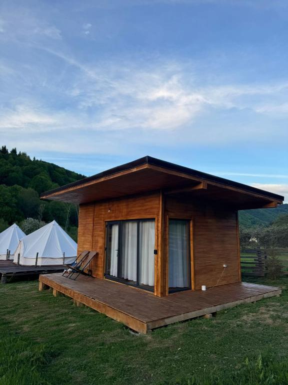 a small cabin with a deck and tents in a field at Glamping - Casuta Zen Fiad in Romuli