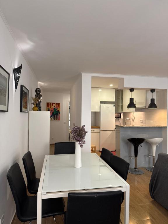 a white dining room table with black chairs and a kitchen at Namaste in Sesimbra