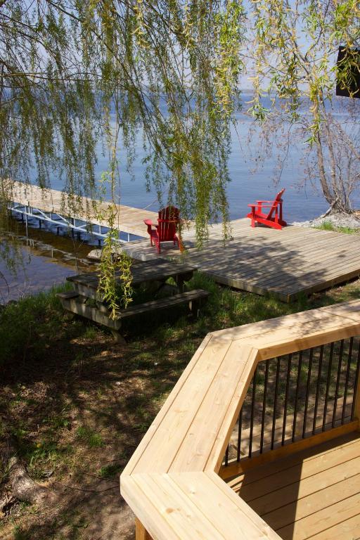 a wooden dock with two red chairs on the water at Tanglewood - Large Waterfront Home in PEC ST-2020-0172 in Waupoos