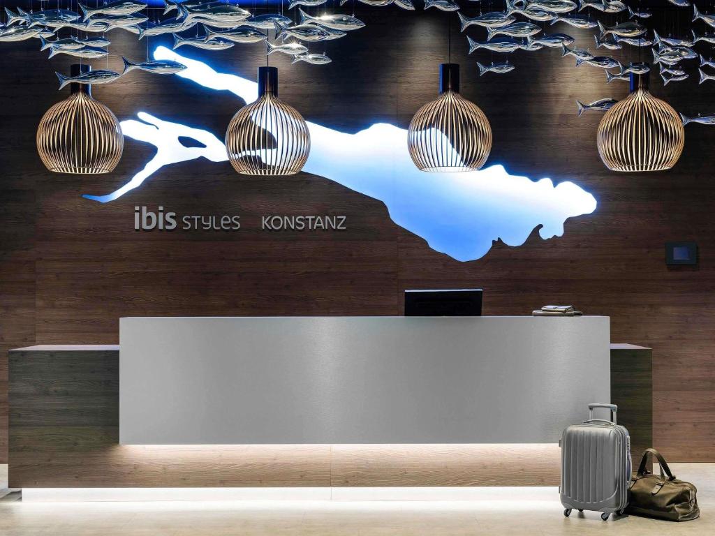 a reception desk with a suitcase and lights at Ibis Styles Konstanz in Konstanz