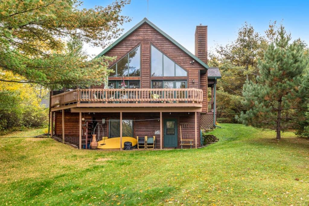 a log house with a deck and a balcony at RTLCMP Lakehouse in Arbor Vitae
