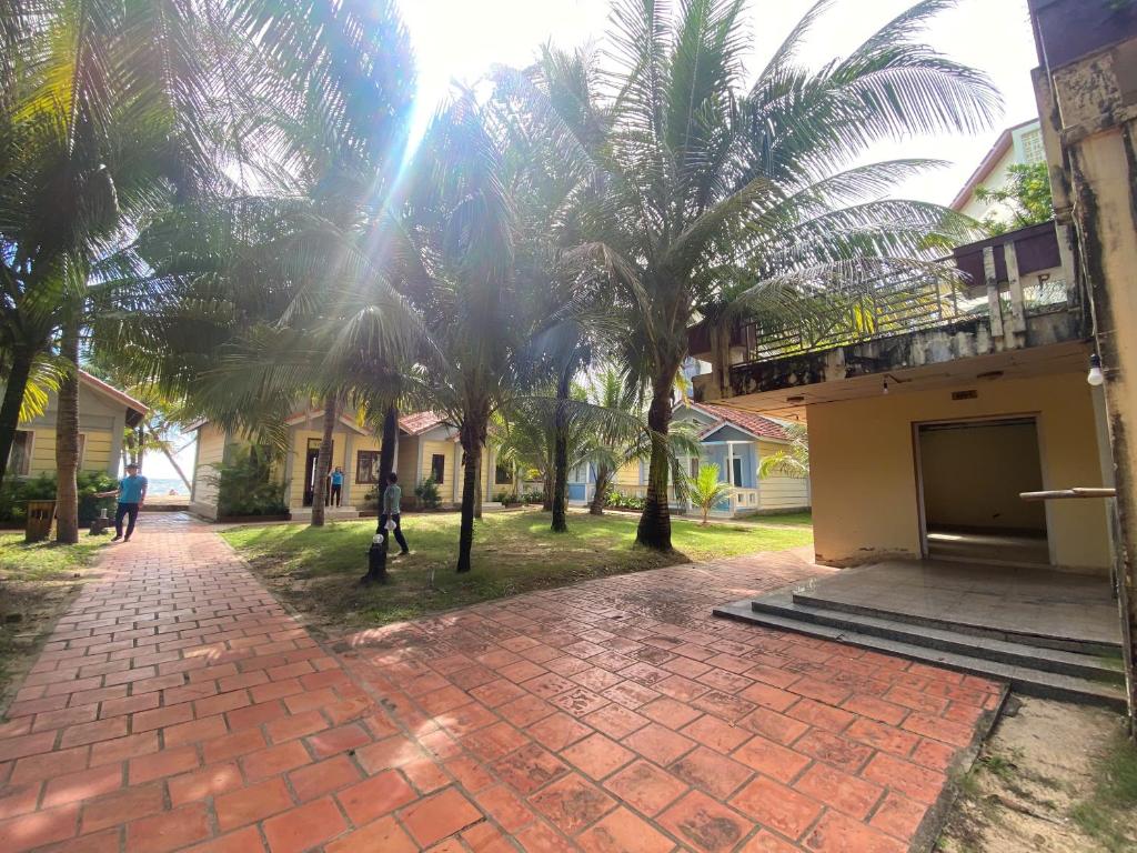 a brick walkway in front of a building with palm trees at Beachfront Bungalow Cuu Long in Phú Quốc