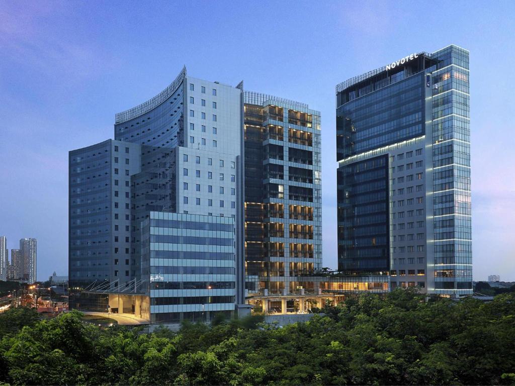 two tall glass buildings in a city with trees at Novotel Samator Surabaya Timur in Surabaya