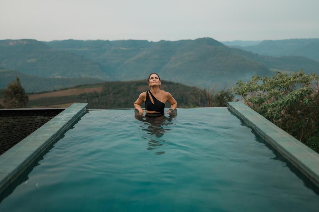 a woman sitting in a swimming pool with mountains in the background at Casas na montanha - Villa Montegrappa in Caxias do Sul