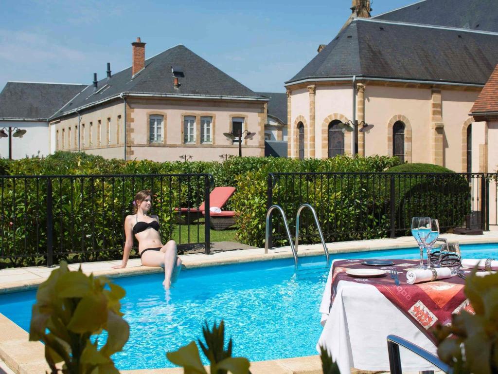 a woman in a black bikini sitting in a swimming pool at Mercure Moulins Centre Hôtel de Paris in Moulins