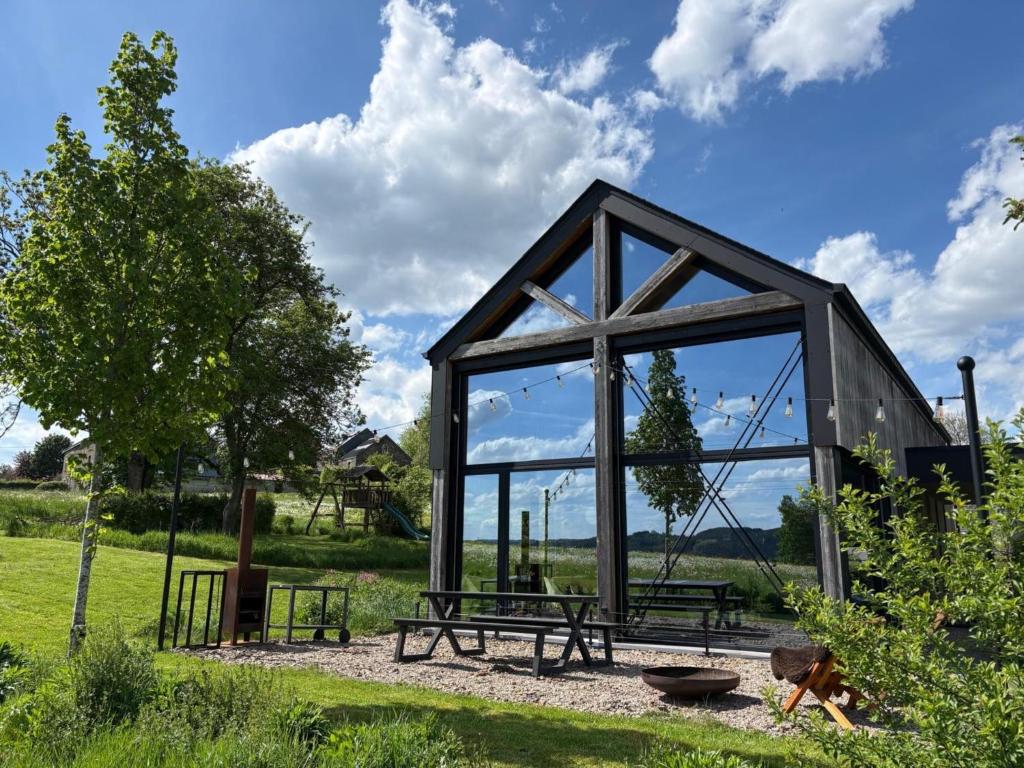 a small greenhouse with benches and a tree in a field at Modern design house with sauna 'Arduenna Silva' in La-Roche-en-Ardenne