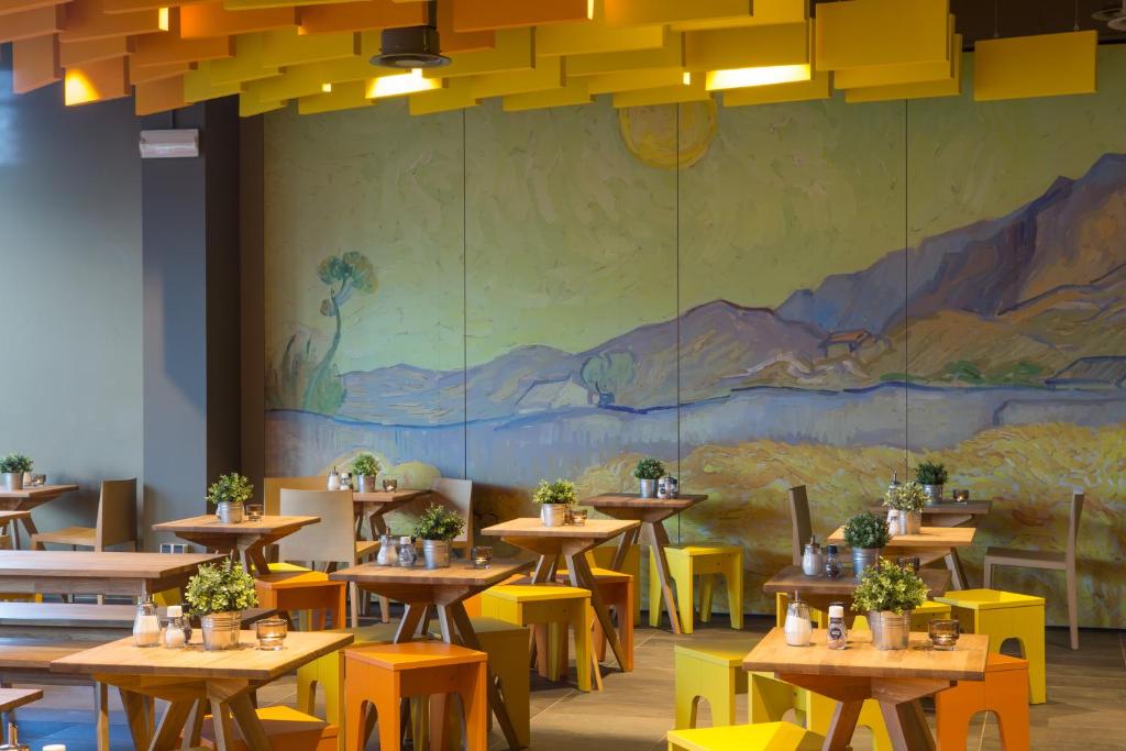 a dining room with tables and yellow chairs and a mural at MEININGER Hotel Amsterdam City West in Amsterdam