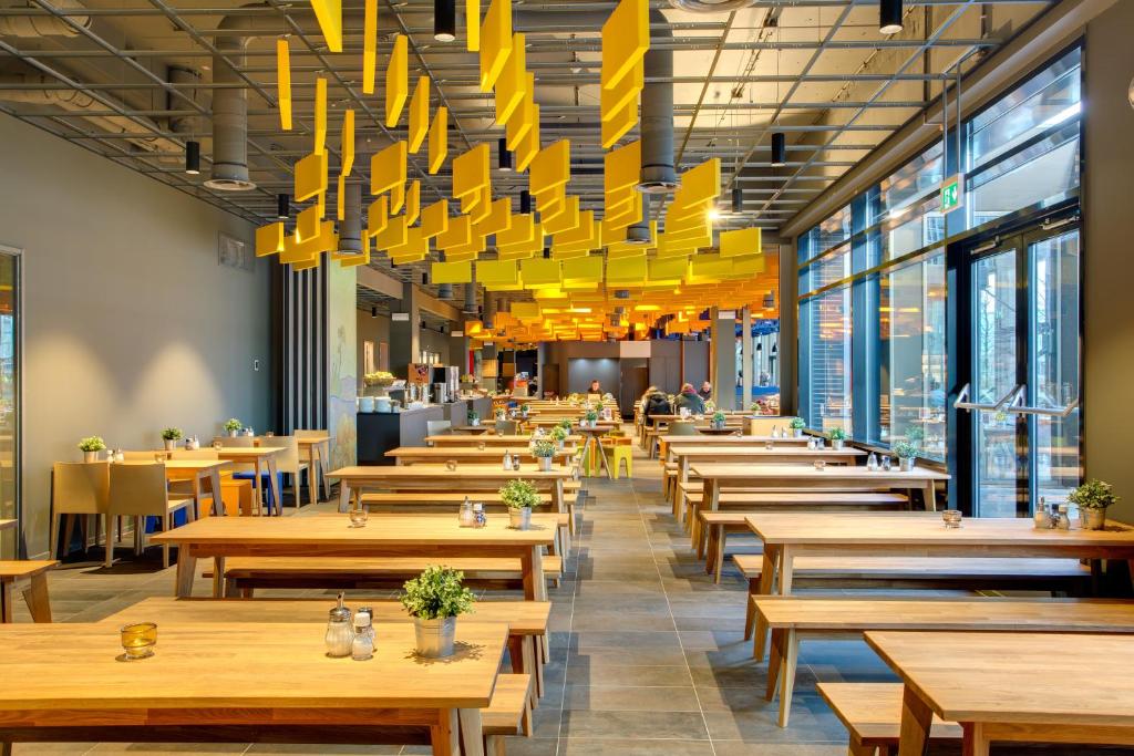 a restaurant with wooden tables and yellow chandeliers at MEININGER Hotel Amsterdam City West in Amsterdam